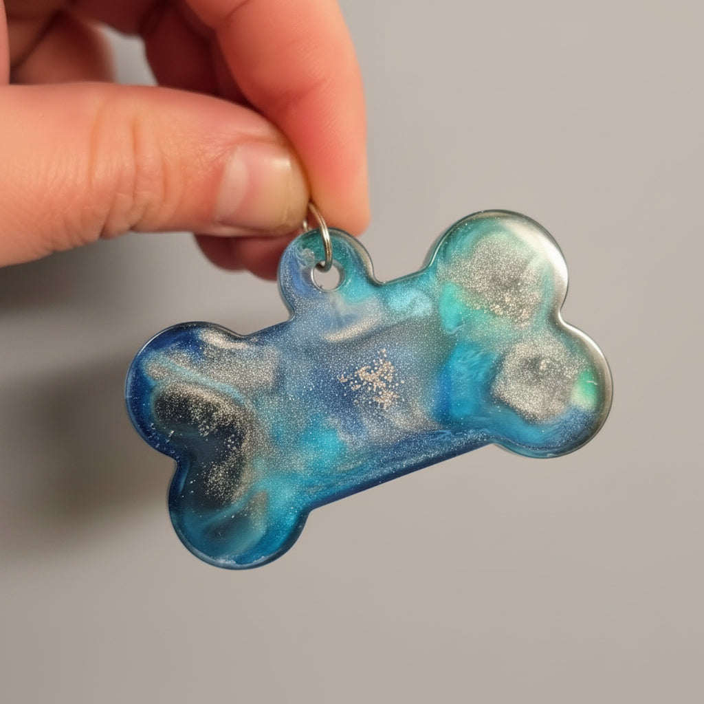 A bone-shaped pet ID tag with a blue, green, and black marbled pattern, held by a hand against a solid purple background.